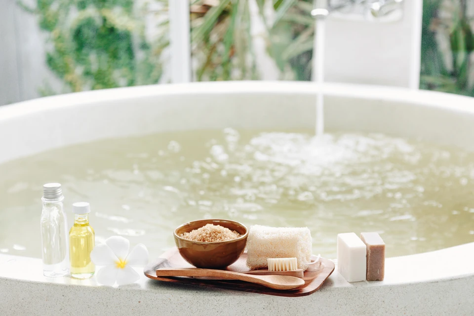 Scène de spa avec baignoire remplie d'eau, produits de bien-être disposés sur plateau en bois au premier plan